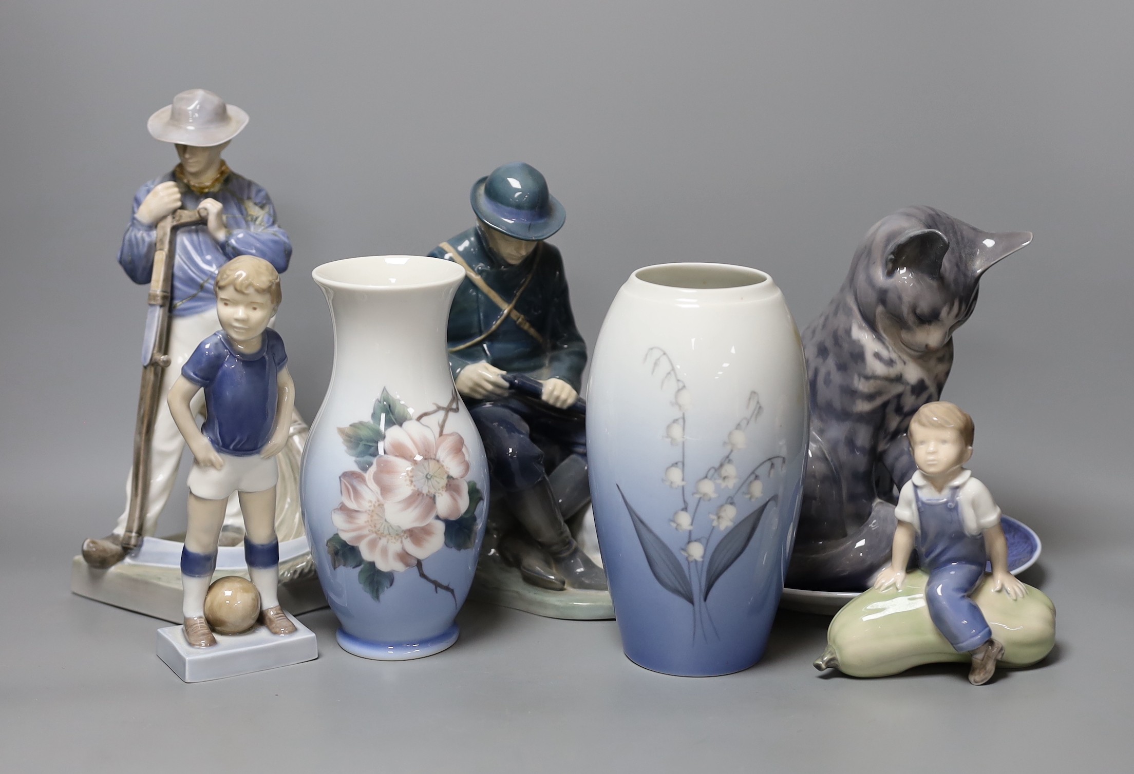 Eight pieces of Royal Copenhagen, to include a seated cat 340, Christmas Rose and Cat plate, a seated farm boy 4539, a young footballer 5657, two floral vases 2630 2289 and 57/251 K.P, a seated huntsman with dog 1087, an